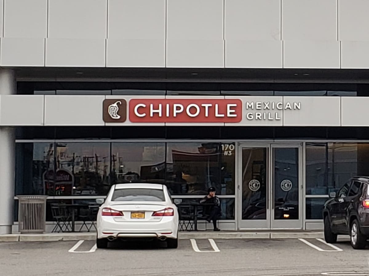 A chipotle restaurant with cars parked in front of it.