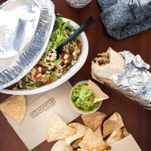 A Chipotle burrito and chips with salsa and guacamole on a table.