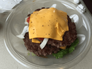 A burger with cheese and lettuce in a plastic container.