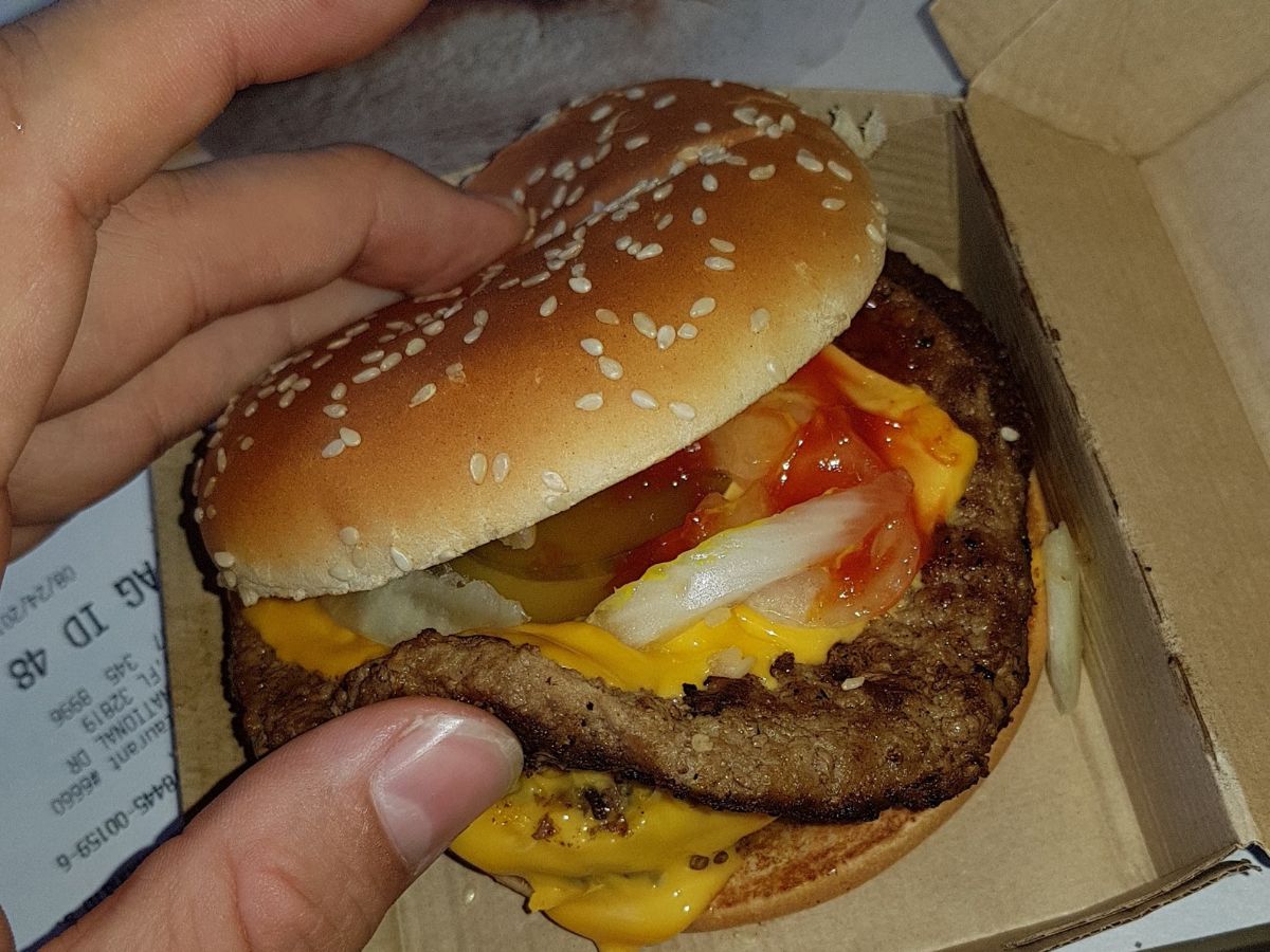 A person holding a McDonald's Double Cheeseburger in a cardboard box.