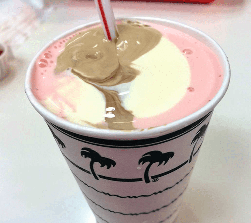 A pink and white milkshake with a straw on top.