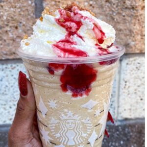 A person holding a starbucks drink with whipped cream and starawberry drizzle