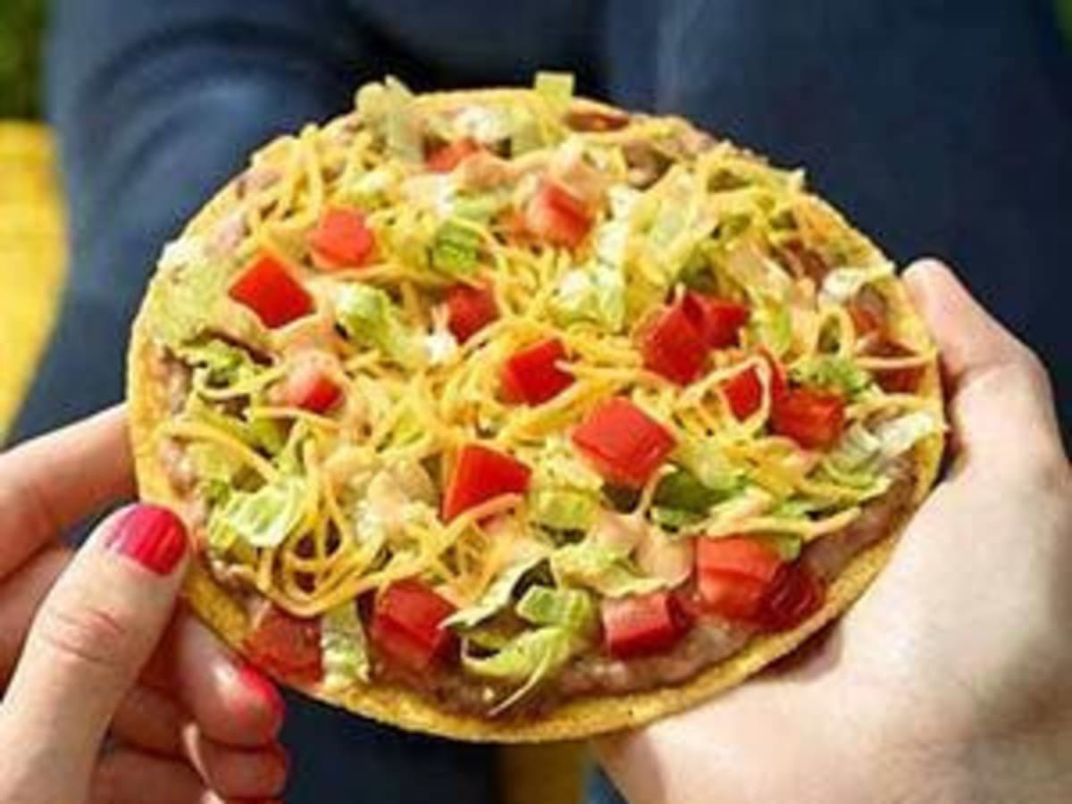 A person holding a small pizza with vegetarian toppings on it.