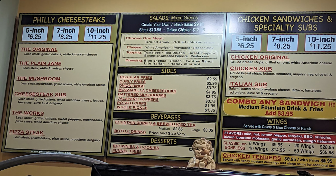 A menu with Philly Connection prices is displayed on a wall in a restaurant.