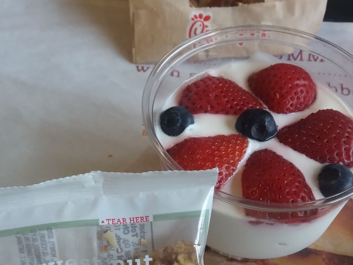 A cup of yogurt with berries and a bag of granola.