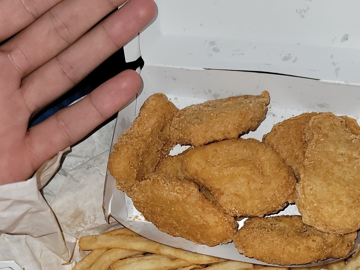 A hand holding a box of french fries and mcdonalds nuggets.