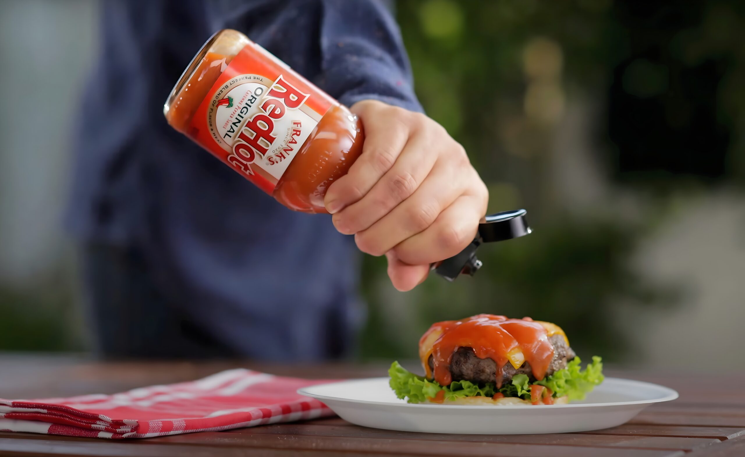 A person is putting sauce on a burger.